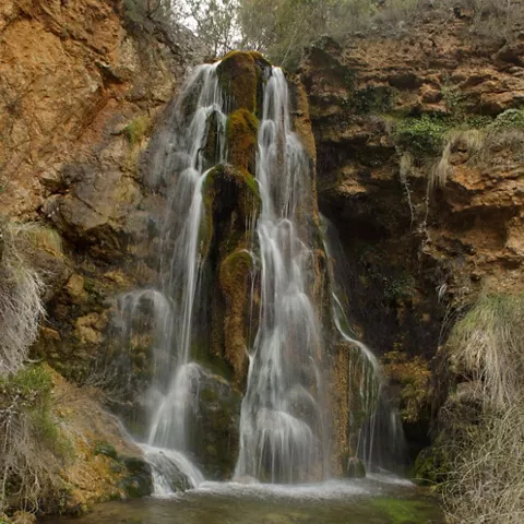 Cascada de agua cayendo sobre formaciones rocosas cubiertas de musgo.
