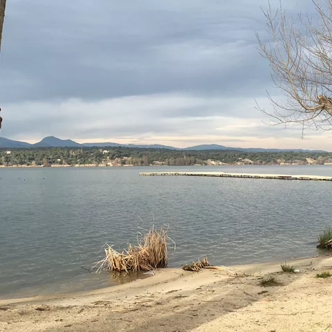 Orilla del embalse con pasarela flotante y paisaje montañoso al fondo