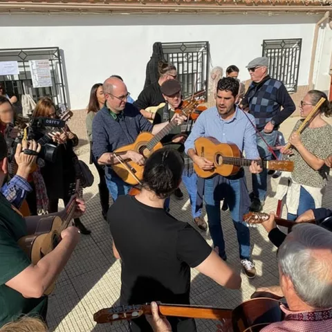 Grupo de músicos tocando guitarras en círculo en una plaza.