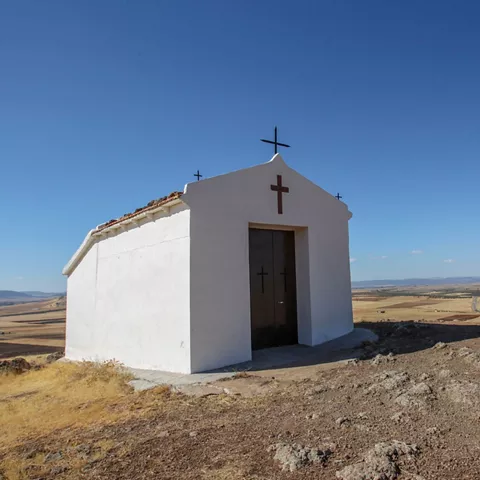 Pequeña ermita blanca con cruz sobre una colina.