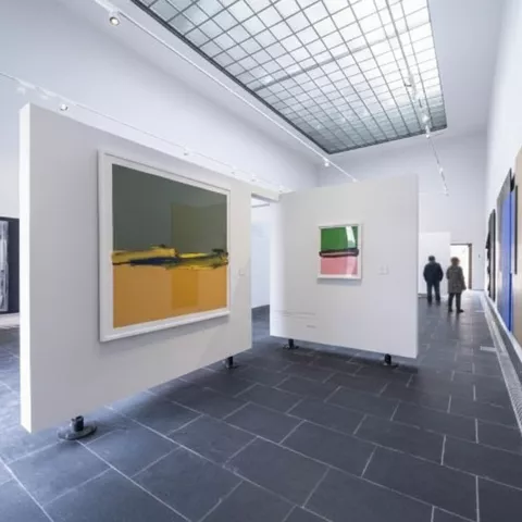 Sala blanca con pinturas abstractas de gran formato y paneles móviles.