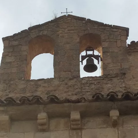 Espadaña de piedra con campana y canecillos.