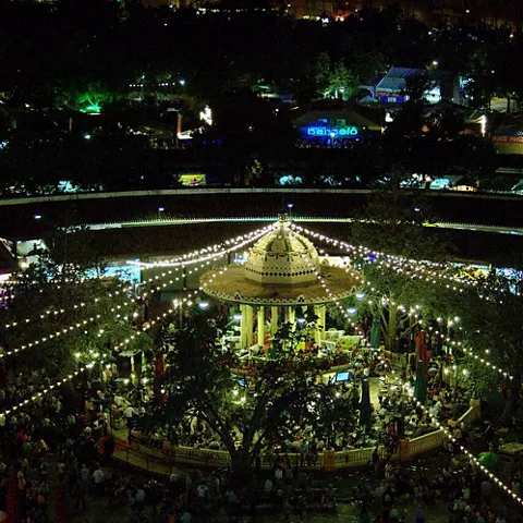 Recinto circular iluminado de noche con templete y ambiente festivo.