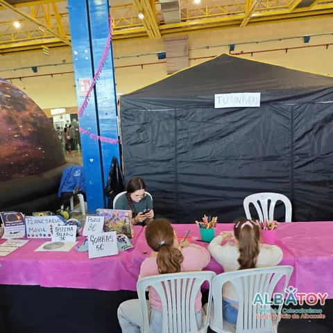 Puesto de actividades con mesa rosa, material de dibujo y una cúpula inflable al fondo.