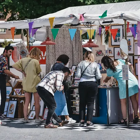 Puesto de mercado con ilustraciones y personas observando productos artesanales.