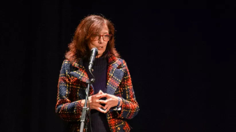 Mujer hablando ante un micrófono sobre un escenario oscuro