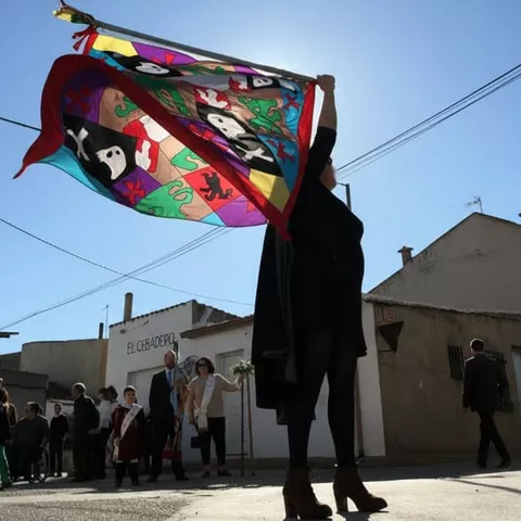 Persona levantando bandera colorida en acto popular al aire libre.
