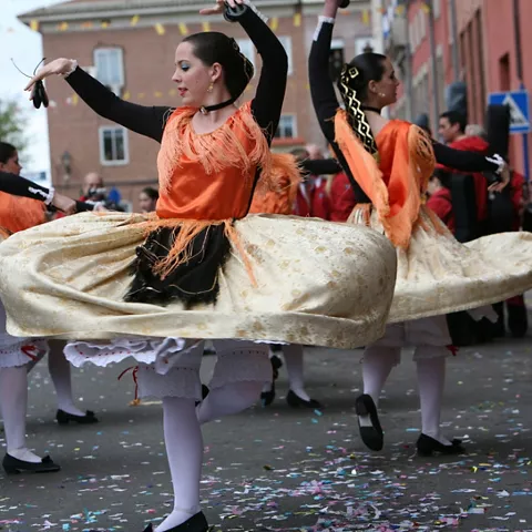 Bailarinas con vestidos tradicionales girando en un desfile festivo.