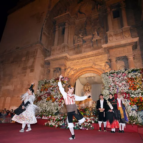 Baile tradicional nocturno frente a una fachada histórica decorada con flores.