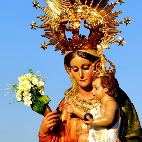 Imagen religiosa coronada con un niño en brazos sobre fondo de cielo azul.