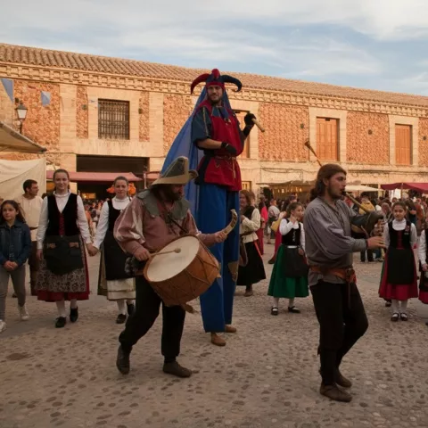 Música y animación en una plaza, con músicos y participantes en trajes tradicionales entre el público.
