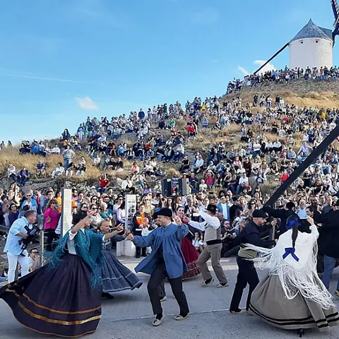 Baile tradicional al aire libre con público numeroso y molinos al fondo.