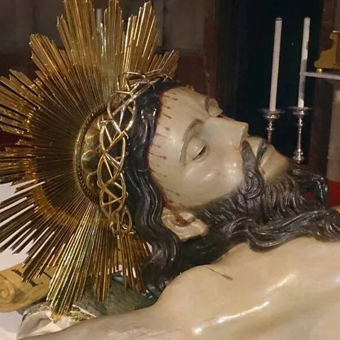 Detalle de escultura religiosa yacente con halo dorado y velas al fondo.