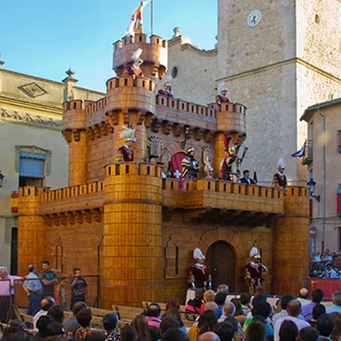Recreación histórica con fortaleza escénica y público en una plaza.