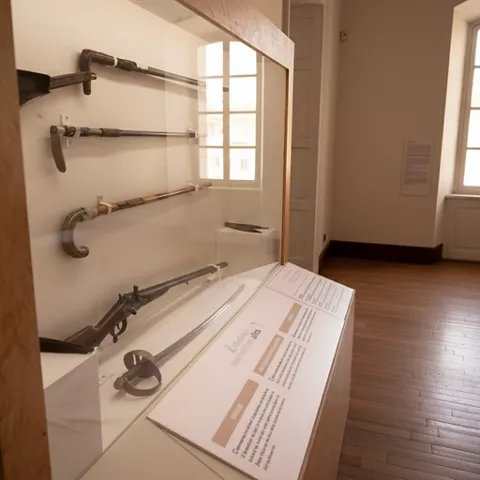 Vitrina de pared con armas antiguas y panel informativo, junto a una ventana.