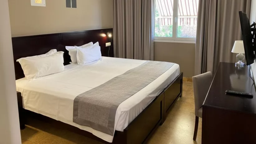 Habitación luminosa con cama doble, escritorio y ventana con cortinas.