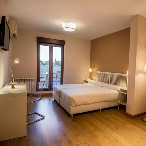 Habitación luminosa con cama doble, balcón acristalado y sillón blanco.