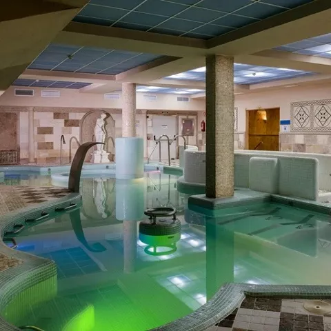 Piscina termal interior con columnas, chorros de agua y revestimiento de mosaico.