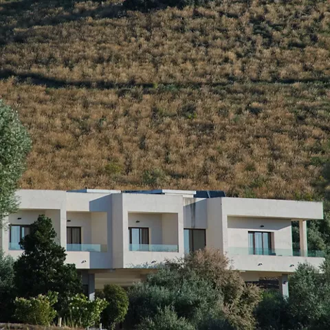 Edificios blancos integrados en una ladera con vegetación y paisaje natural alrededor.