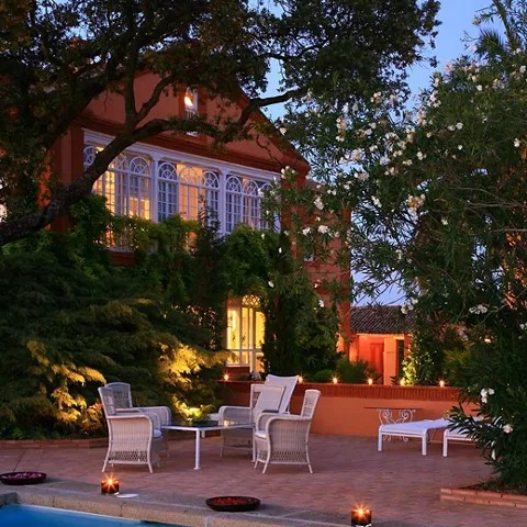 Piscina exterior iluminada frente a un edificio rodeado de árboles