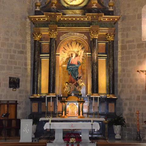 Retablo dorado con imagen central elevada sobre un altar en un templo de piedra.
