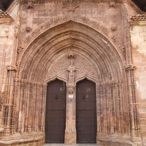 Portada gótica de piedra con arco apuntado, relieves tallados y dos puertas de madera.