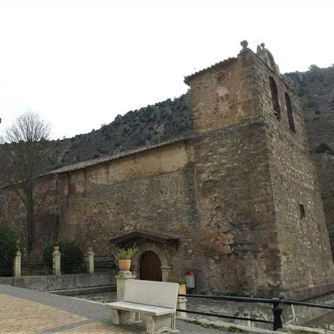 Iglesia de piedra en una plaza con farola y banco.