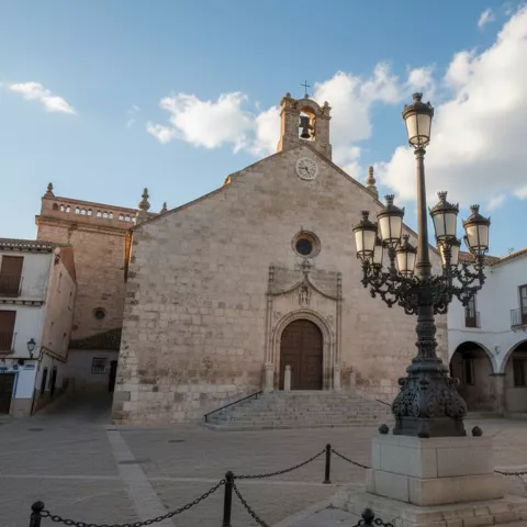 Iglesia de piedra en una plaza con farola central y soportales laterales.