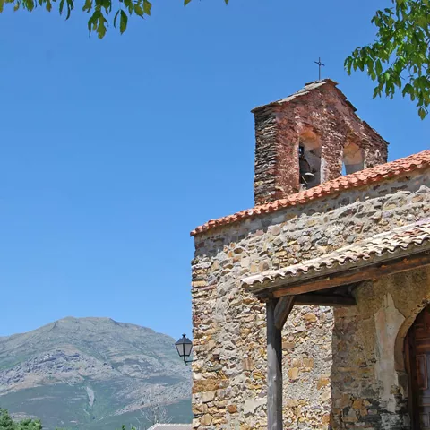 Detalle de campanario y entrada de iglesia con paisaje montañoso.
