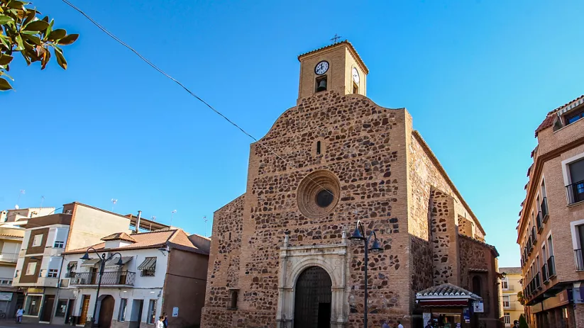Iglesia parroquial de piedra con torre del reloj en la plaza.