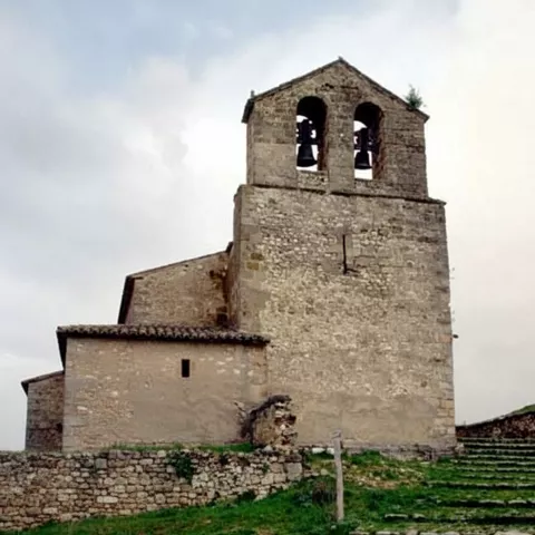 Iglesia rural de piedra con espadaña y escalinata de acceso en ladera verde.
