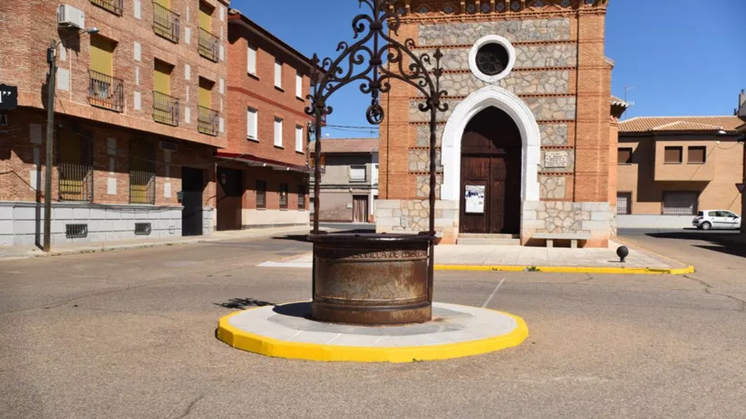 Pozo metálico decorativo en primer plano con iglesia de ladrillo al fondo.