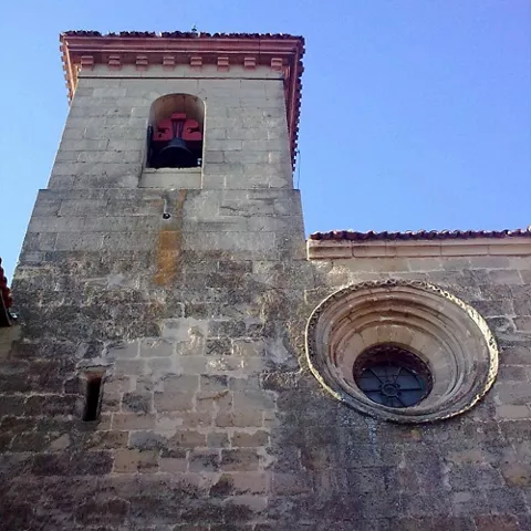 Campanario y óculo en fachada de piedra bajo cielo azul.