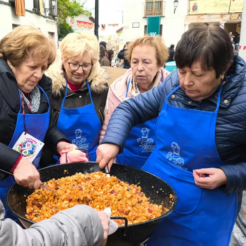 Grupo de personas con delantales azules removiendo comida en una sartén grande al aire libre.