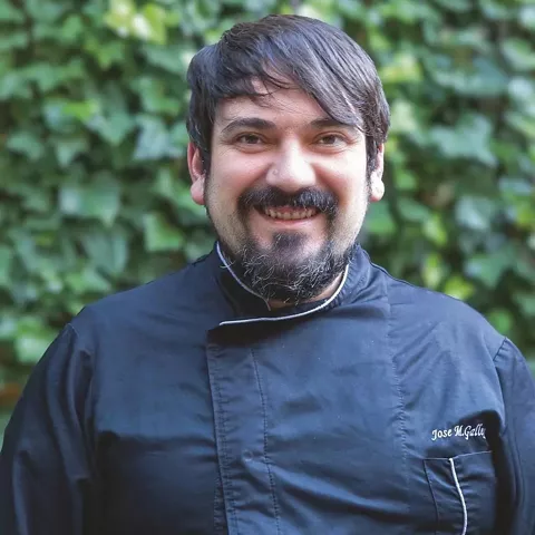 Retrato de cocinero con chaqueta negra ante un fondo vegetal