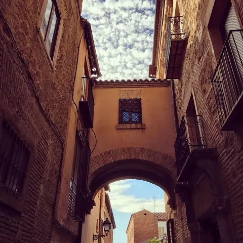 Calle estrecha con casas antiguas, balcones de hierro y arco entre edificios.