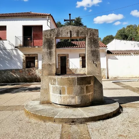 Pozo de piedra en una plaza con casas blancas