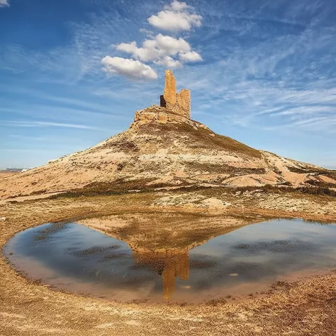 Ruinas fortificadas sobre colina reflejadas en charca