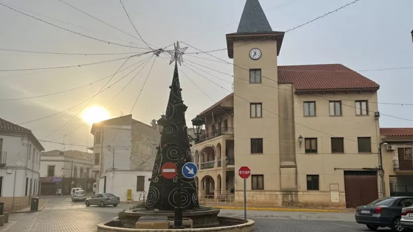 Plaza de Madrigueras con árbol decorativo y edificio municipal con torre del reloj al atardecer.