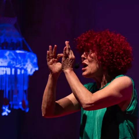 Actriz con micrófono bajo luz escénica.