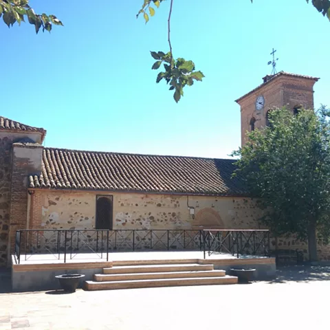Iglesia de piedra y ladrillo con torre y plaza soleada