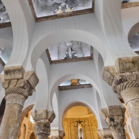 Detalle interior de columnas y arcos blancos bajo techos abovedados.