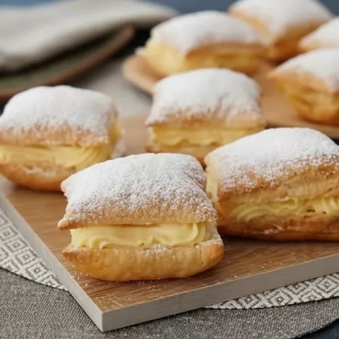 Pasteles pequeños rellenos de crema sobre una tabla de madera.