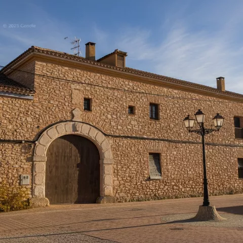 Edificio tradicional de Minaya con fachada de piedra y puerta de madera en una plaza tranquila.