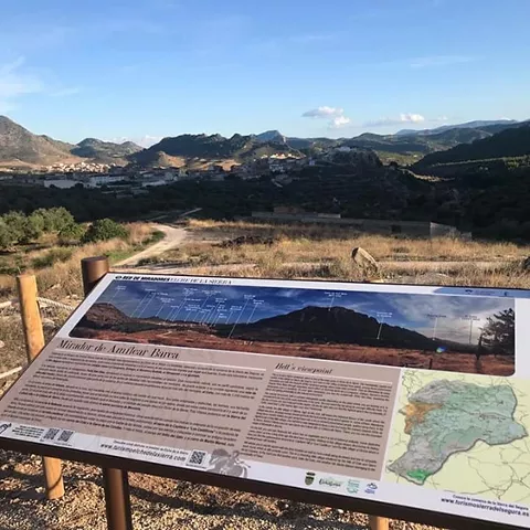 Panel informativo en un mirador con vistas a un valle y montañas.