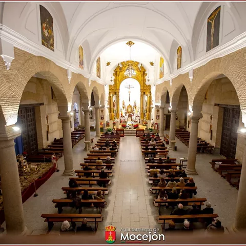 Interior de iglesia con arcos de ladrillo, bancos y altar iluminado