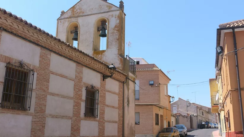 Calle junto a iglesia con campanario de dos vanos y nido en la parte superior