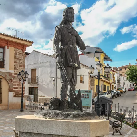 Monumento escultórico en una plaza con fuente y bancos.