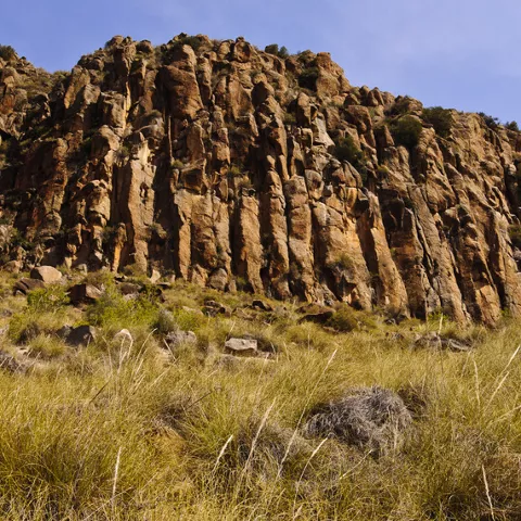 Formación rocosa escarpada con columnas naturales y vegetación baja en primer plano.