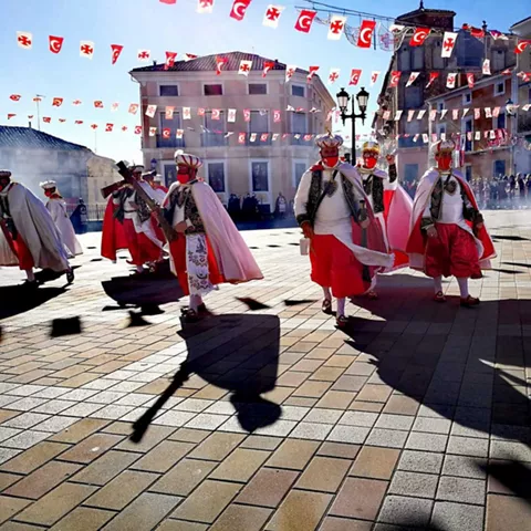 Desfile festivo con personas vestidas con trajes tradicionales y banderines.